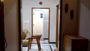 Un pasillo con una silla de madera y un sofá al fondo, que conduce a una habitación con una puerta.