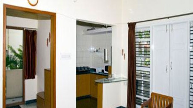 Habitación de hotel con kitchenette, comedor con mesa y sillas, y baño con ducha e inodoro.