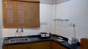 Una cocina compacta con un lavamanos, armarios de madera, una encimera negra, un tostador y un estante de vidrio.