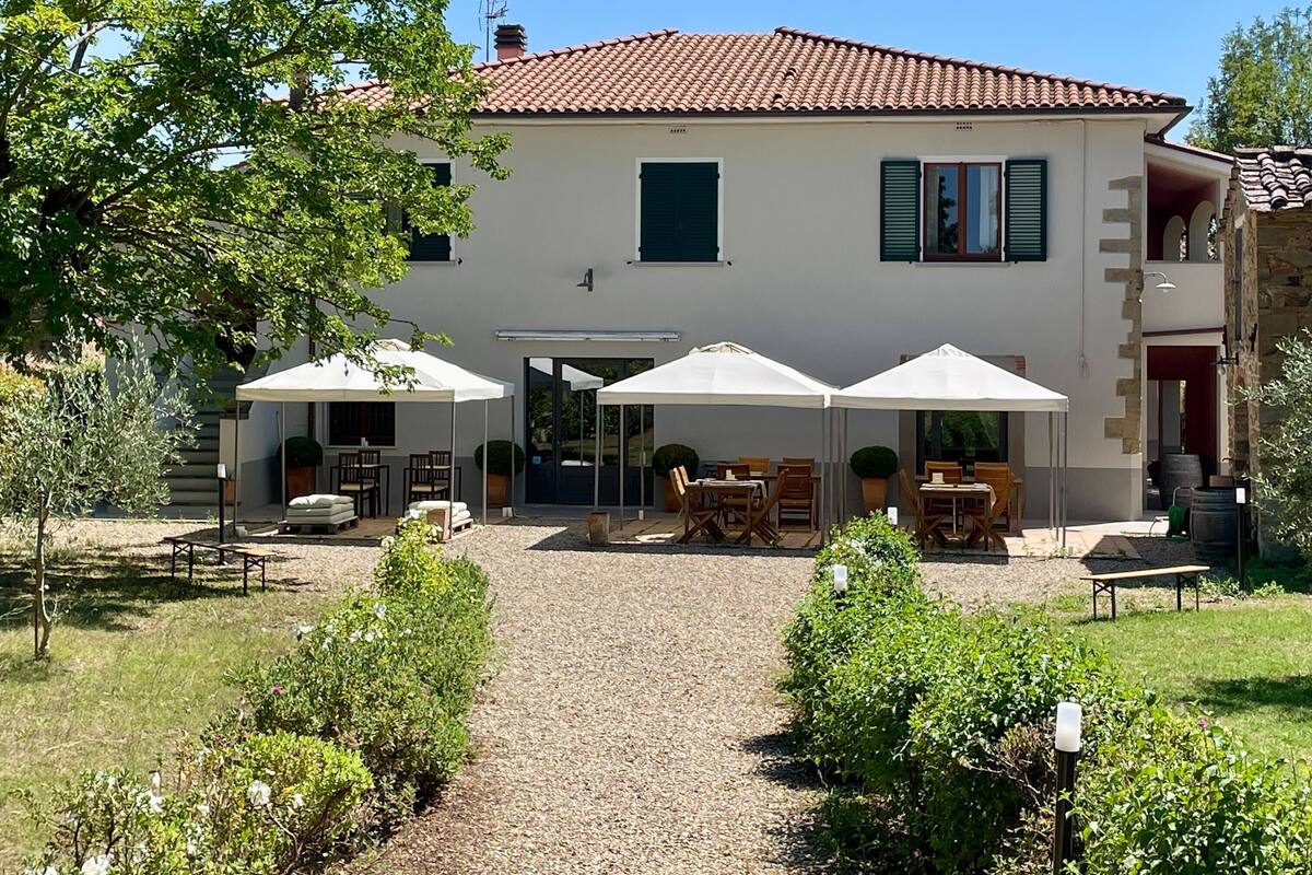 Ein zweistöckiges Haus mit Ziegeldach, einer überdachten Terrasse mit Gartenmöbeln und einem Schotterweg.