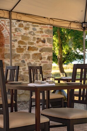 A table set for four with chairs, a stone wall, and a tree in the background.