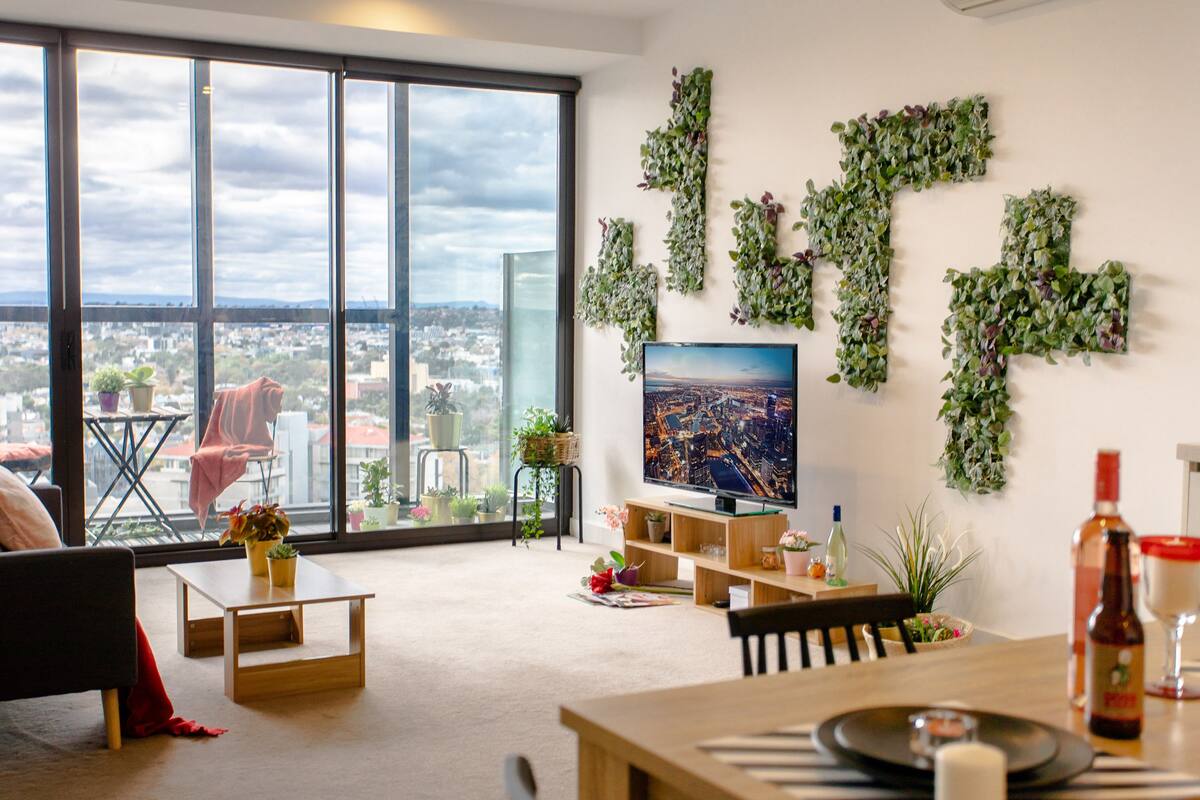 Un salon moderne doté d’une grande fenêtre, d’un téléviseur à écran plat et offrant une vue sur le paysage urbain.