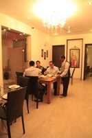 A dining area with a chandelier, a glass partition, and a painting on the wall.
