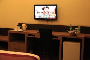 Una habitación de hotel con una cama, un escritorio, una silla, un televisor, un refrigerador y dos botellas de agua.