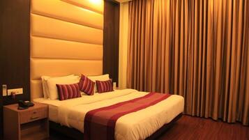 Habitación de hotel con una cama grande, una mesita de noche, un teléfono y una ventana con cortinas.