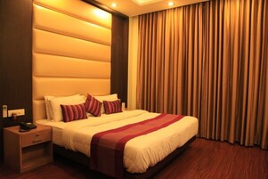 Habitación de hotel con una cama grande, una mesita de noche, un teléfono y una ventana con cortinas.