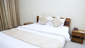 A neatly made bed with a patterned bedspread and pillows, a bedside table with a telephone, and a curtain with a swirl pattern. - Hotel Golden City (Sylhet)