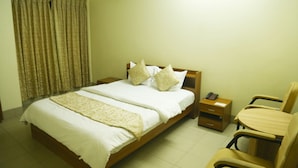 A neatly made bed with a white and beige bedspread, a wooden headboard, and two bedside tables with a lamp and a phone. - Hotel Golden City (Sylhet)
