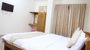 A neatly made bed with a wooden frame and white bedding, a television mounted on the wall, a wardrobe with a mirror, and a patterned curtain. - Hotel Golden City (Sylhet)