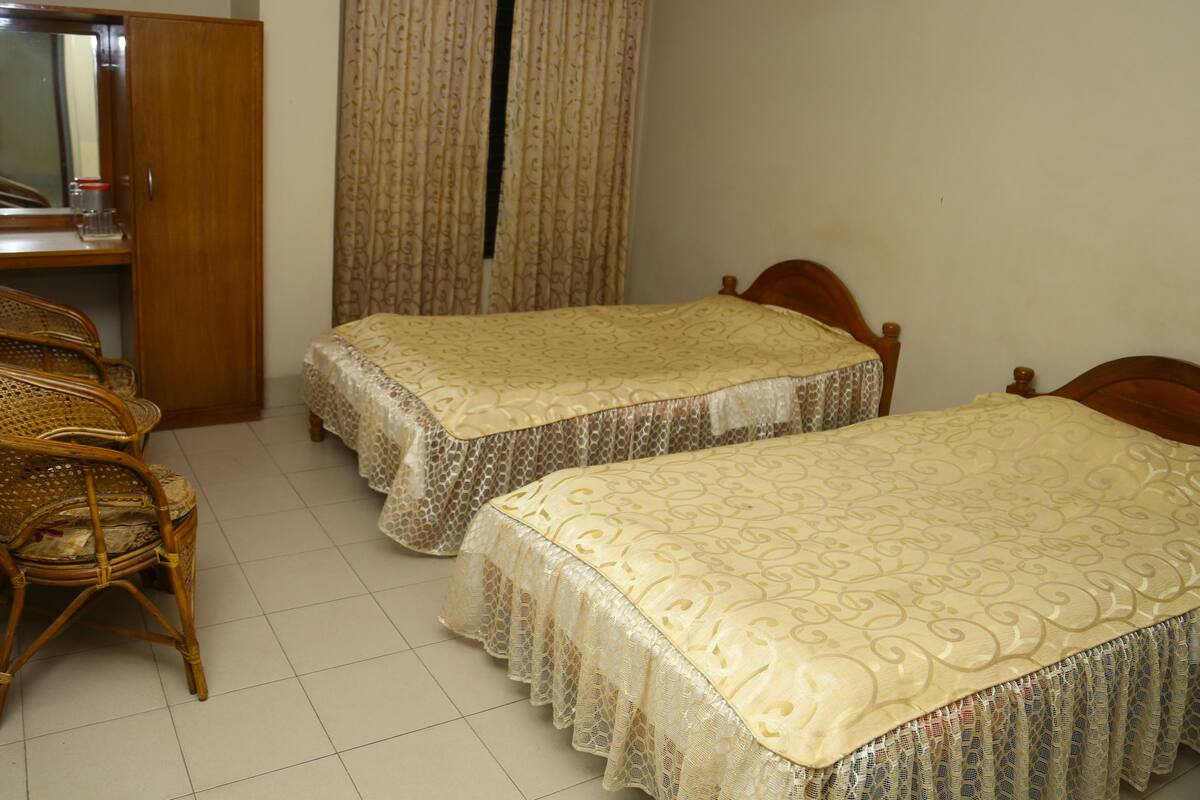 A room with two single beds, a wooden wardrobe, a wicker chair, and a curtain.