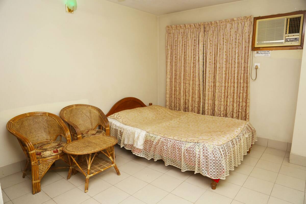 A room with a bed, two wicker chairs, a small table, a curtain, and a wall-mounted air conditioning unit.