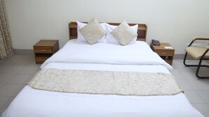 A neatly made bed with a patterned bedspread, two pillows, and a bedside table with a phone and a lamp. - Hotel Golden City (Sylhet)
