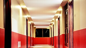 Un long couloir étroit aux murs rouges et blancs, doté d’un sol à motifs et d’un plafond pourvu d’un éclairage encastré.