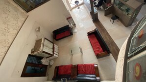 Une pièce spacieuse avec un plafond haut, une grande fenêtre, un lit recouvert d’une couverture rouge, un bureau avec un ordinateur et un aquarium.