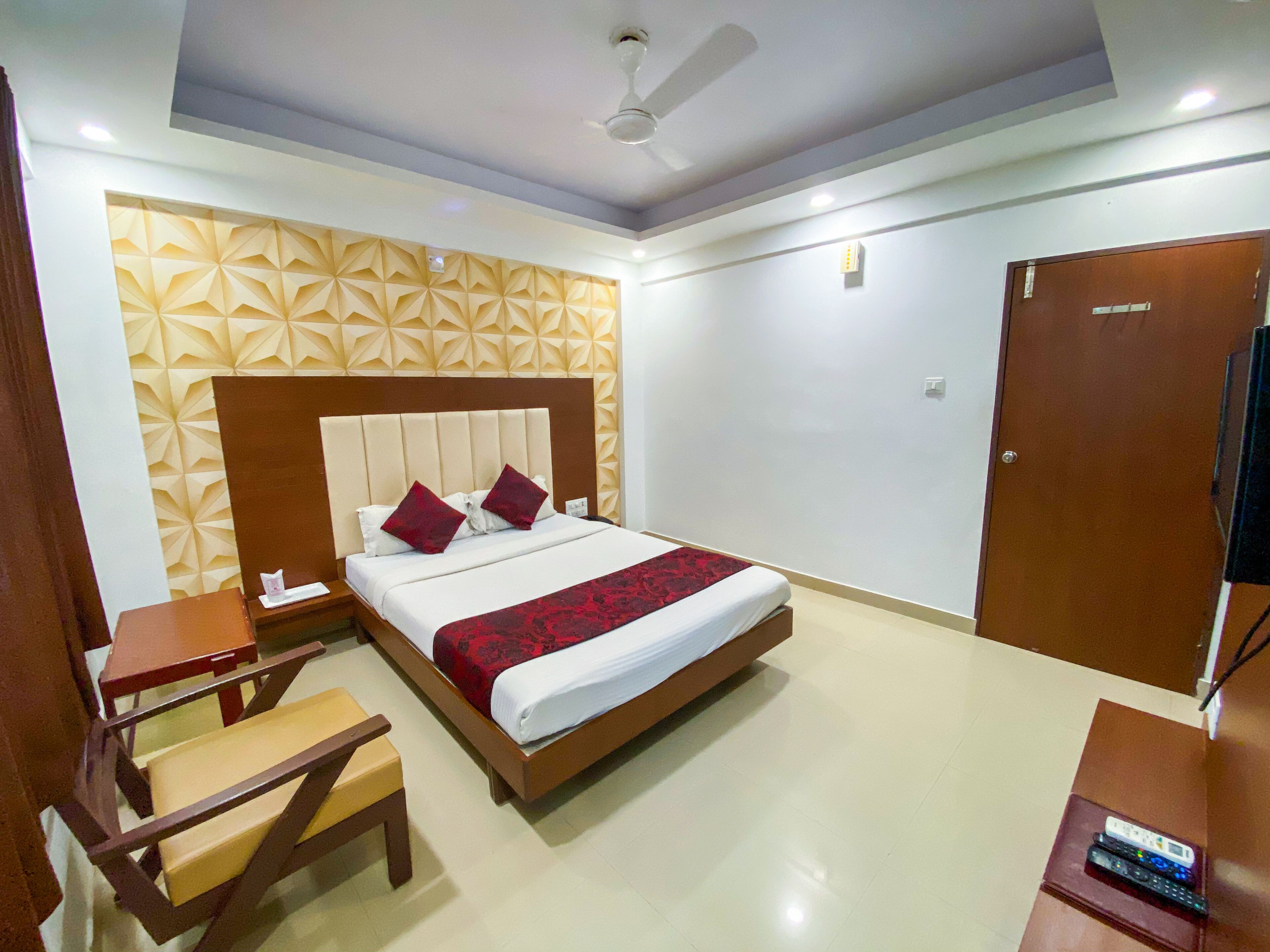 A hotel room with a bed, a wooden nightstand, a chair, a wardrobe, and a ceiling fan.