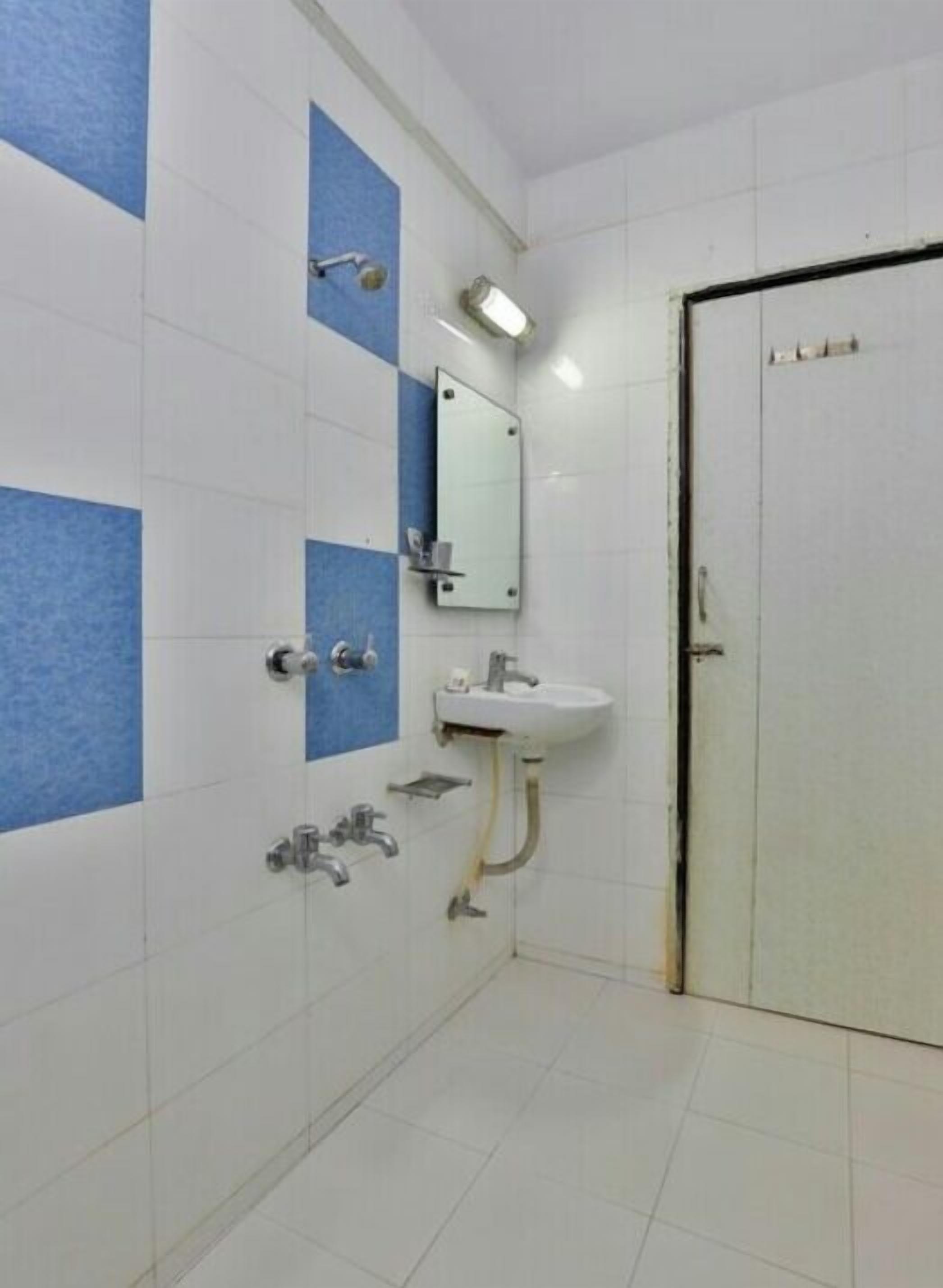 Casa de banho com azulejos brancos e azuis, uma pia, um espelho e uma porta.