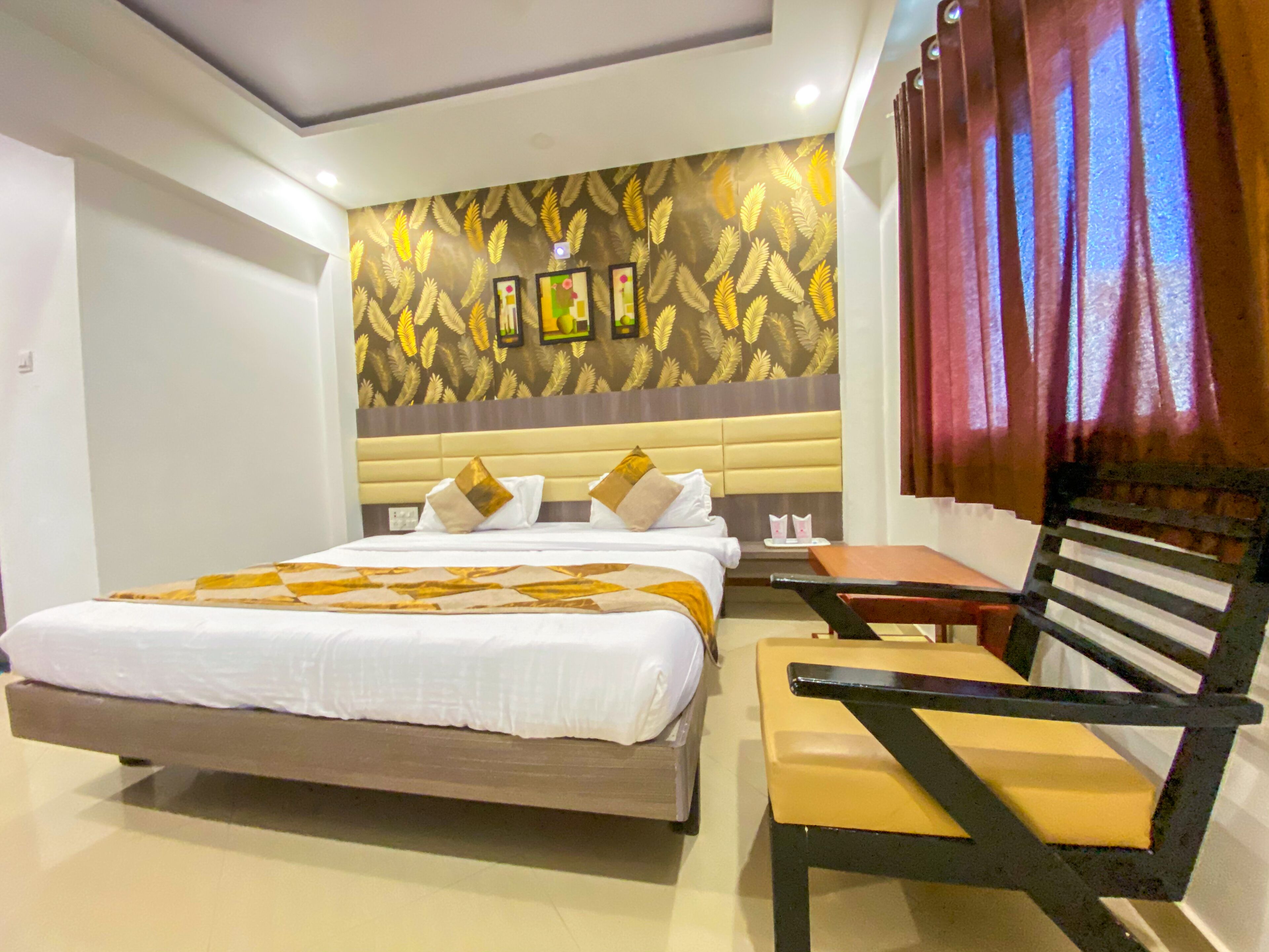 Habitación de hotel con una cama grande, una mesita de noche, una silla y una pared decorativa con motivos de hojas.