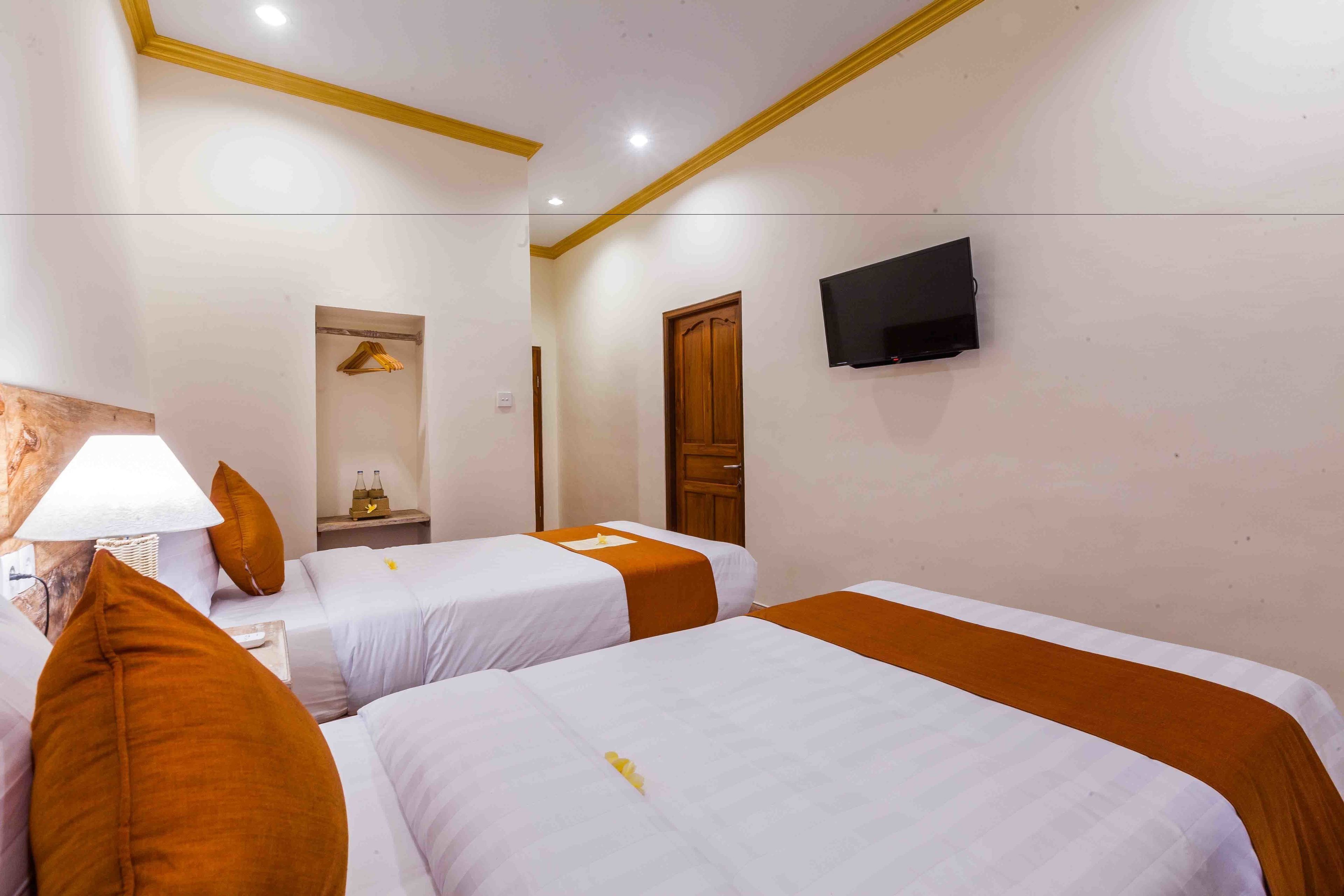 A hotel room with two beds, a TV mounted on the wall, a lamp, and a wooden door.