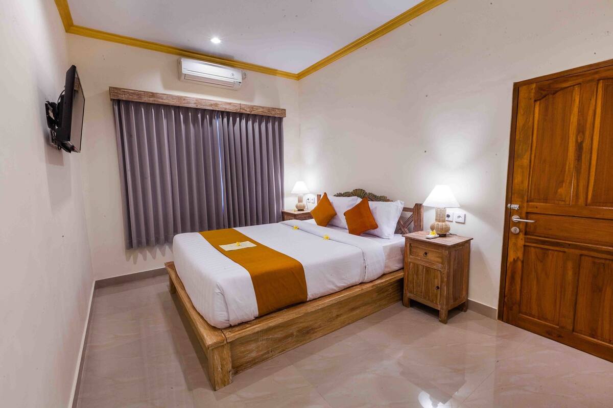 Une chambre à coucher bien rangée, avec un lit, des lampes de chevet, une table de chevet en bois, une armoire et un téléviseur fixé au mur.