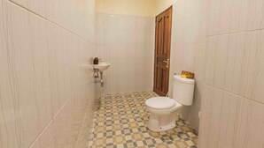 A bathroom with a checkered floor, a toilet, a sink, and a wooden door. - Vimala Ubud Hotel (Ubud)