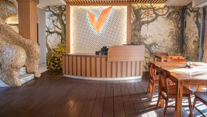 A reception area with a wooden reception desk, a large decorative animal sculpture, and a mural with a tree and landscape. - Vimala Ubud Hotel (Ubud)