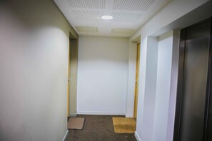 A narrow hallway with white walls, a ceiling with recessed lighting, and a door on the right. - The Nook Serviced Apartment (London)