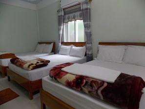 A hotel room with two single beds, each with white linens and a wooden headboard. There is a window with patterned curtains, and a small wooden table is visible in the foreground. - Rose Hotel (Phong Nha)