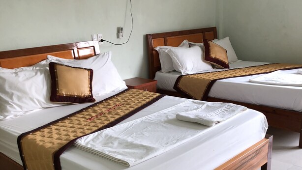 Dos camas de madera con ropa de cama blanca y cabeceros marrones, una mesita de noche y un enchufe en la pared.