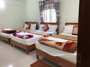 A hotel room with four wooden beds, each with white linens and decorative pillows. - Rose Hotel (Phong Nha)
