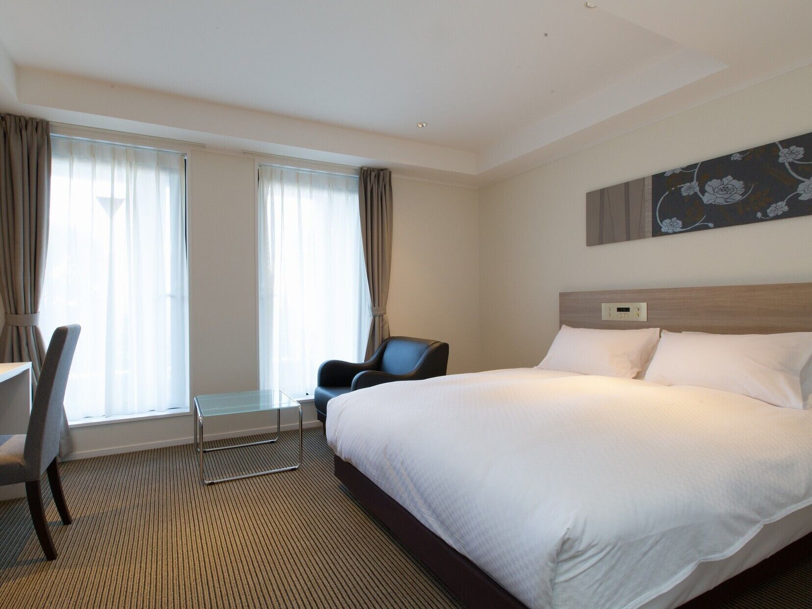 A hotel room with a large bed, a desk, a chair, and a window with curtains.