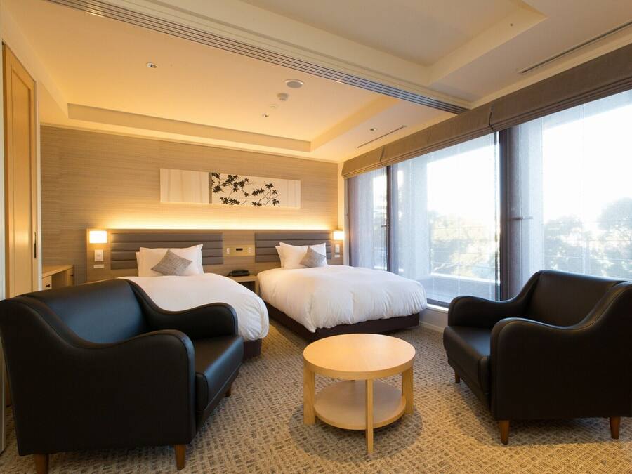 A hotel room with two beds, a round table, and two armchairs.