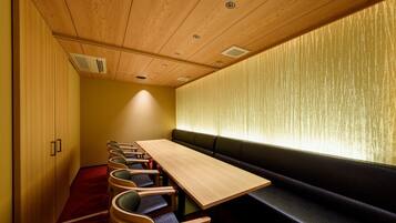 A conference room with a long table and several chairs, a bench along the wall, and a wooden ceiling with recessed lighting.