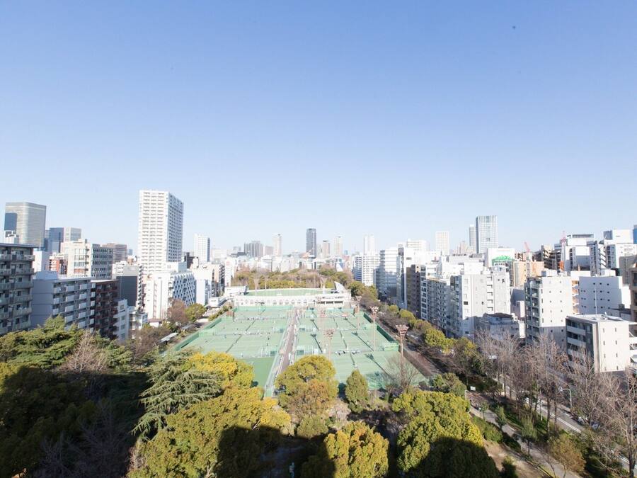 A cityscape with high-rise buildings, a large green sports field, and surrounding trees.
