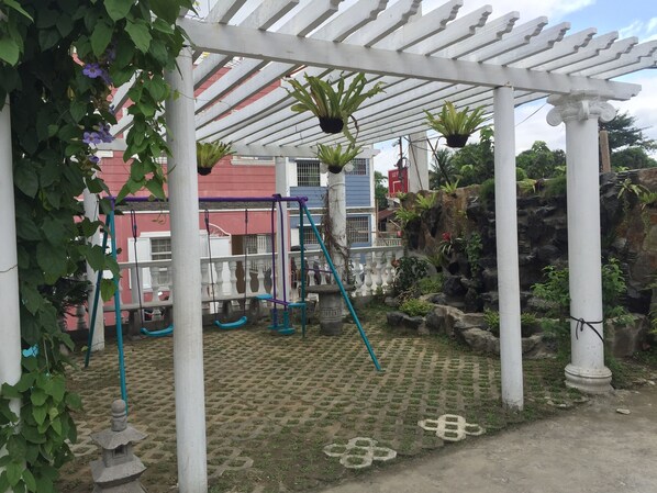Un espacio al aire libre cubierto con una pérgola, columpios y plantas en macetas.