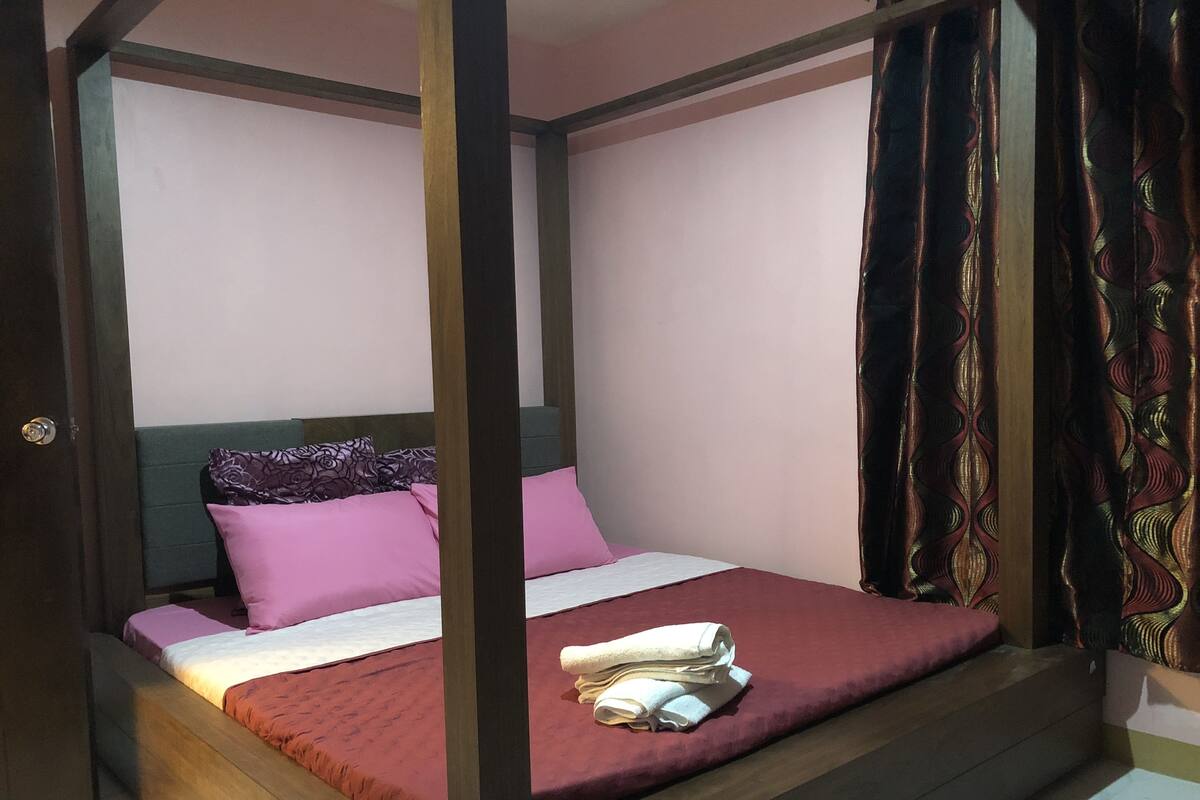 A four-poster bed with a wooden frame, a red bedspread, and multiple pillows.