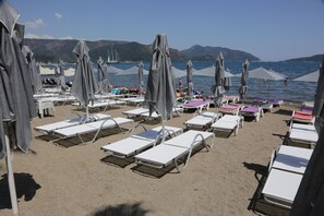 A beach with rows of sunbeds and umbrellas, a clear sky, and a body of water in the background.
