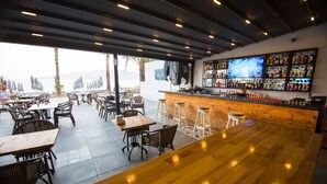 A bar area with wooden tables and chairs, a bar counter with stools, and a large TV screen on the wall. - Geo Beach Hotel Marmaris (Marmaris)
