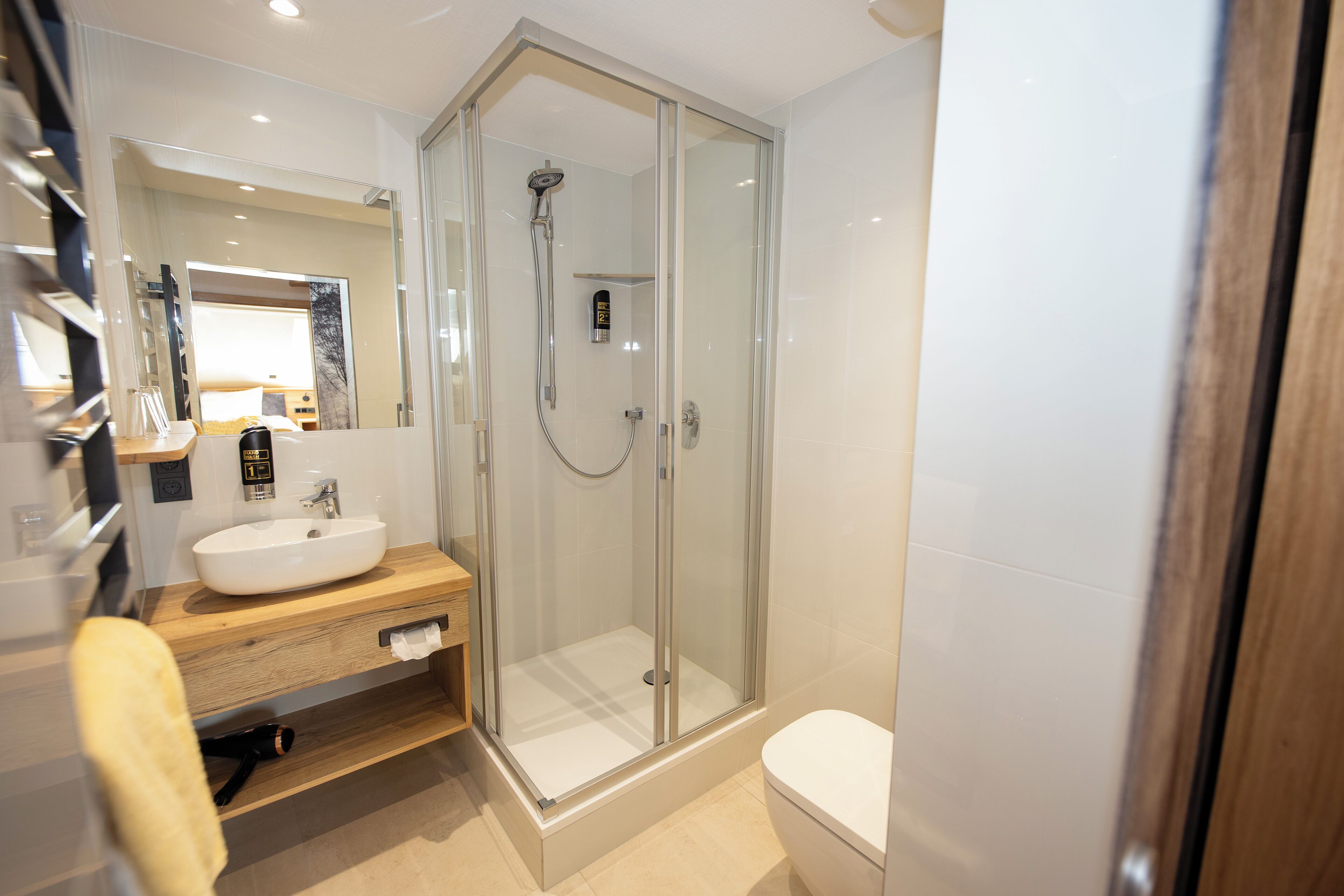 A modern bathroom with a glass-enclosed shower, a wooden vanity, and a white toilet.