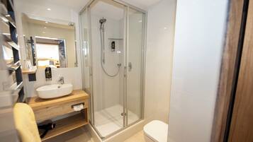 A modern bathroom with a glass-enclosed shower, a wooden vanity, and a white toilet.