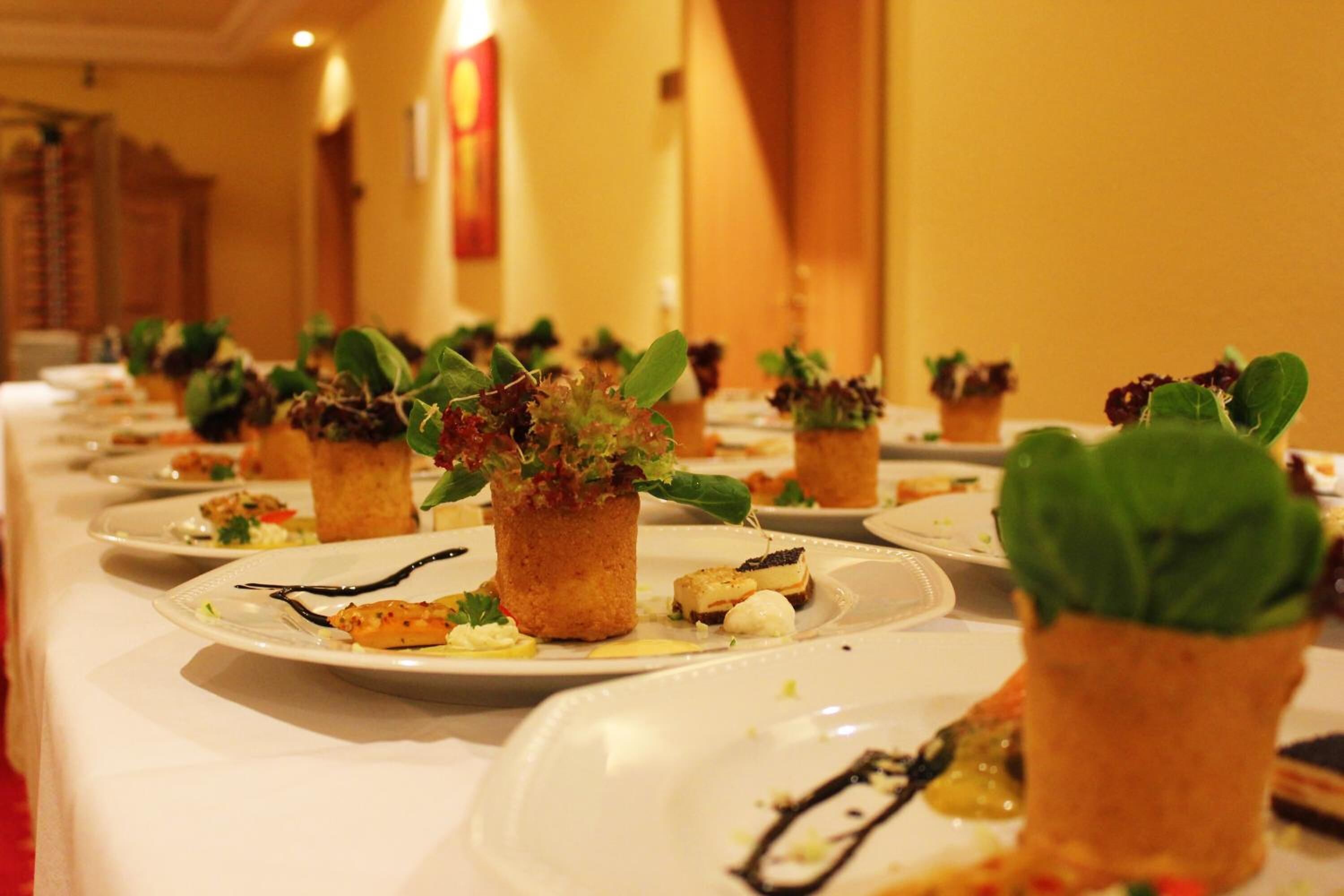 Een lange tafel met meerdere borden eten, elk versierd met een kleine plant.