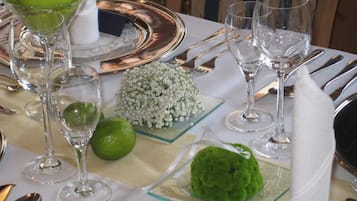Una mesa dispuesta con cristalería transparente, cubiertos y objetos decorativos, incluyendo una fruta verde, un pequeño ramo y un objeto esférico verde.