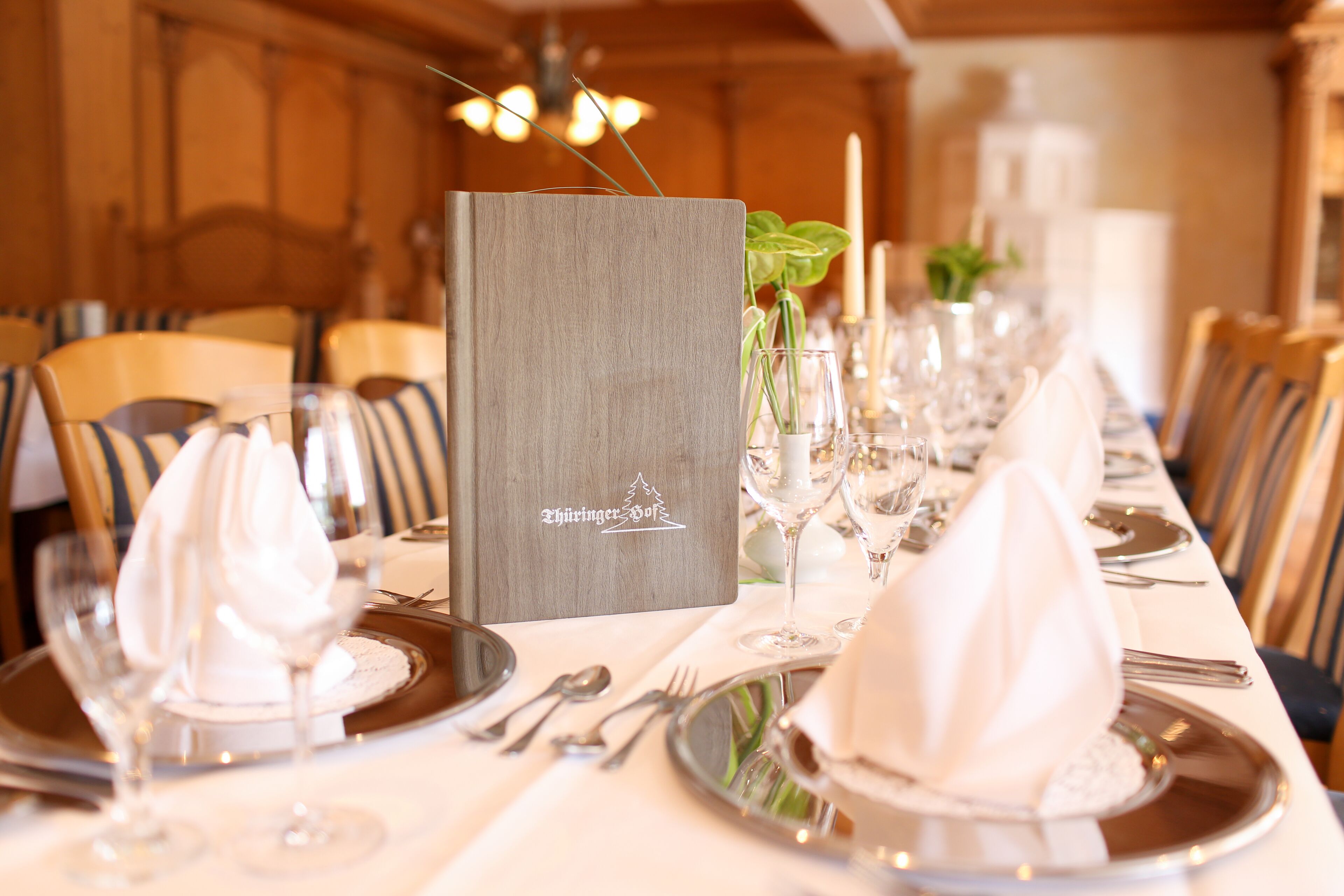 Une table à manger élégante, dressée avec des serviettes blanches, des couverts en argent et des verres à vin, et un présentoir à menus placé au centre.