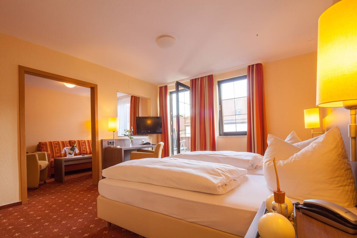 A hotel room with a bed, desk, TV, and a view of the outside.