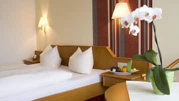 A hotel room with a bed, pillows, a bedside table with a fruit plate, a lamp, and an orchid plant.