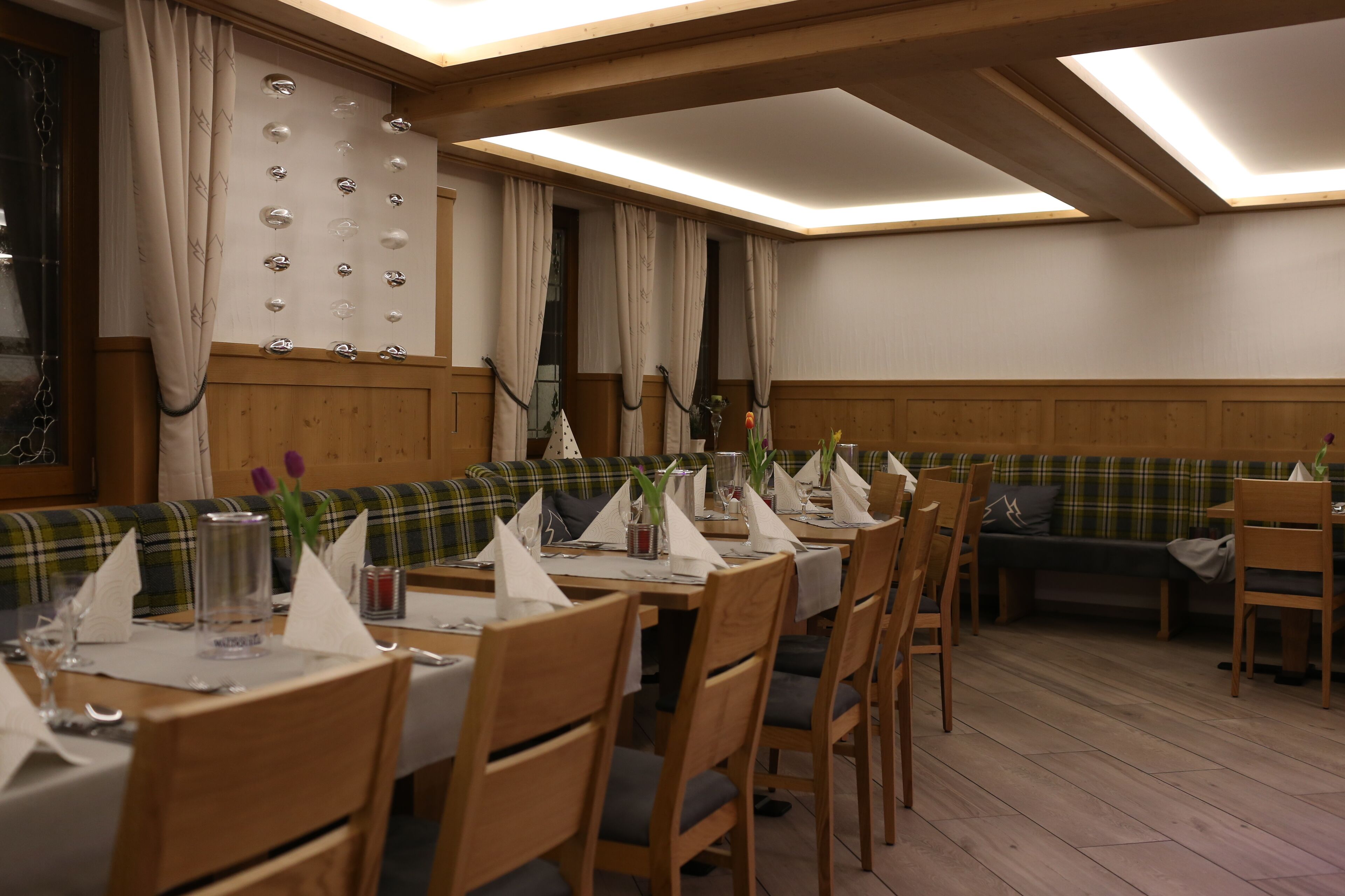 Ein Restaurant mit Holztischen, einem langen Esstisch und einer gemütlichen Sitzecke mit einer Couch und Sesseln.