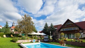A pool area with a clear sky, a large tree, and a building with a red roof. - Hotel-Gasthof Thüringer Hof (Floh)