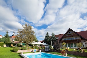 A pool area with a clear sky, a large tree, and a building with a red roof.