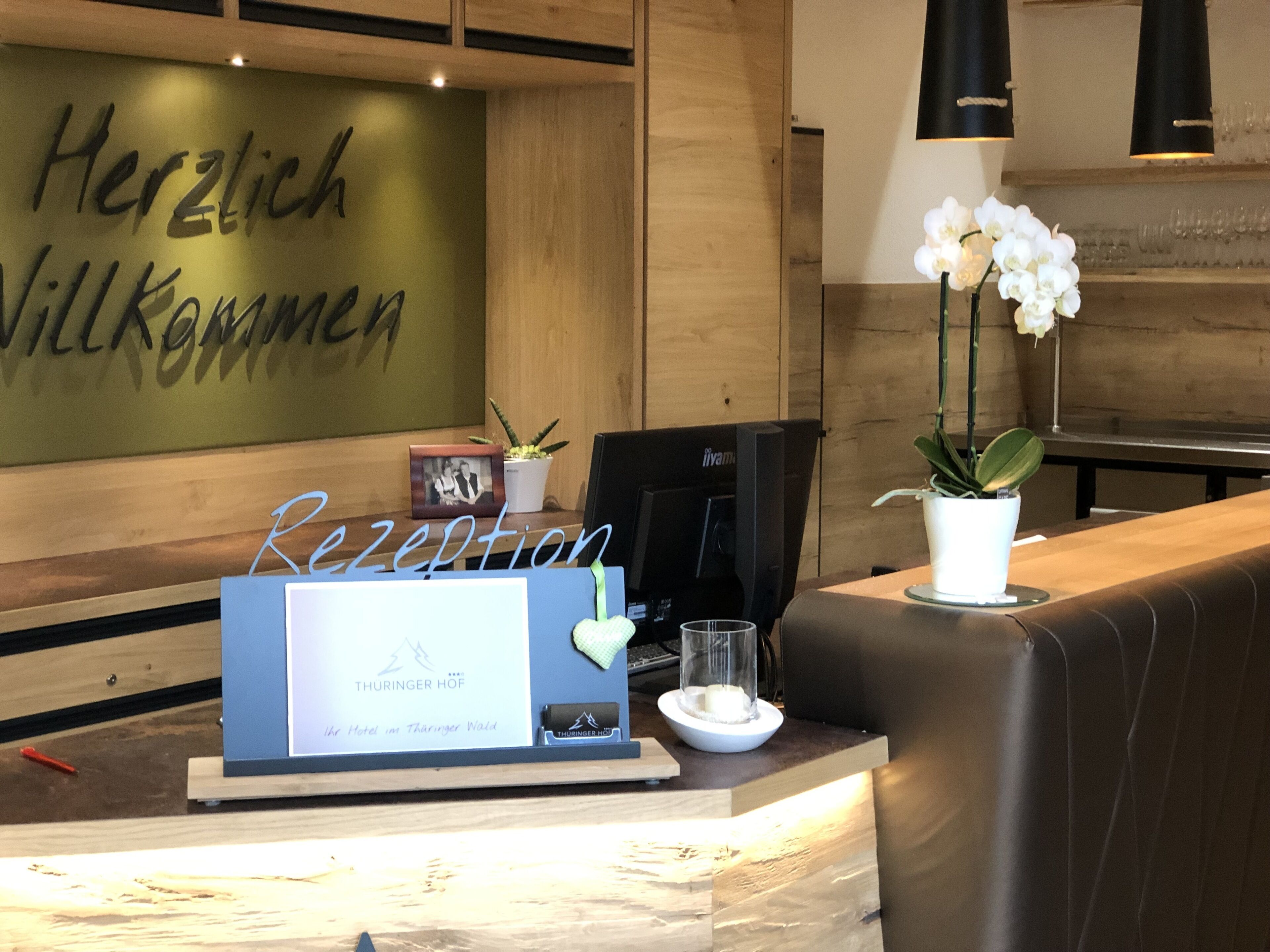 A reception desk with a sign reading "Herzlich Willkommen" and a framed photo on the wall.