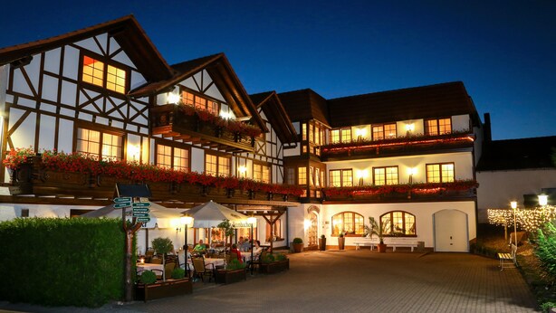 A traditional European hotel with multiple floors, outdoor seating, and a well-lit facade. - Hotel-Gasthof Thüringer Hof (Floh)