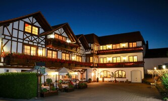 Un hotel tradicional europeo con varios pisos, terraza exterior y fachada bien iluminada.
